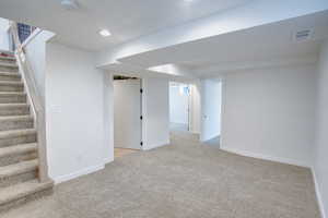 Finished below grade area featuring light carpet, visible vents, baseboards, stairs, and recessed lighting