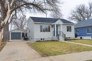 Bungalow featuring an outbuilding, roof with shingles, a front yard, a garage, and driveway