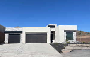 Contemporary house featuring an attached garage, stone siding, concrete driveway, and stucco siding
