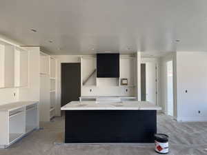 Kitchen featuring a kitchen island, white cabinets, exhaust hood, and unfinished concrete flooring