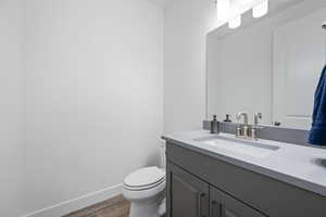 Half bath featuring baseboards, vanity, toilet, and wood finished floors