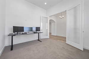 Carpeted office space featuring baseboards, arched walkways, and a chandelier