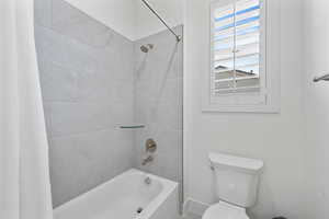 Bathroom with baseboards, toilet, and shower / tub combo with curtain