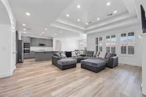 Living area featuring a raised ceiling, visible vents, light wood-style flooring, and a healthy amount of sunlight