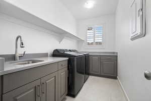 Clothes washing area with cabinet space, baseboards, separate washer and dryer, and a sink