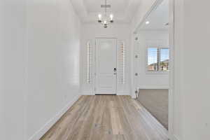 Entrance foyer featuring a chandelier, visible vents, light wood-style floors, baseboards, and a raised ceiling