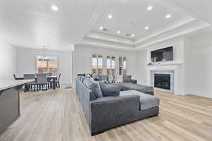 Living room featuring light wood finished floors, a tray ceiling, and a tiled fireplace