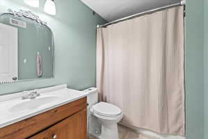 Full bathroom featuring toilet, a textured wall, vanity, and visible vents