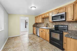 Kitchen featuring stone tile floors, a double sink, appliances with black and stainless steel finishes, and decorative backsplash