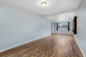 Large family room featuring plenty of natural light, a vaulted ceiling, wood-style vinyl floors, and baseboards