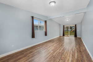 Large family room featuring plenty of natural light, a vaulted ceiling, wood-style vinyl floors, and baseboards