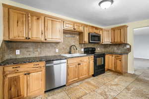 Kitchen with stone tile floors, appliances with black and stainless steel appliances, tasteful backsplash, and a double sink