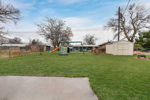 View of of the fenced back yard with a playground and a shed.