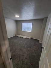 Empty room with a textured ceiling, dark carpet, and baseboards