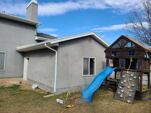 View of side of property with a yard, a chimney, a playground, and stucco siding