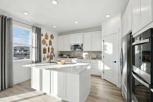 Kitchen with light countertops, a kitchen island with sink, white cabinetry, stainless steel appliances, and decorative backsplash