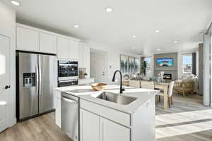 Kitchen with light wood-type flooring, appliances with stainless steel finishes, a kitchen island with sink, a sink, and open floor plan
