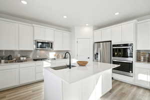 Kitchen featuring white cabinetry, backsplash, stainless steel appliances, light wood finished floors, and a sink