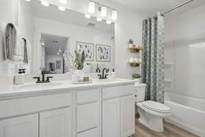 Bathroom with toilet, double vanity, a sink, and visible vents