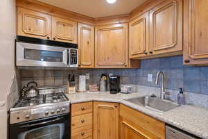 Kitchen with appliances with stainless steel finishes, backsplash, a sink, and light countertops