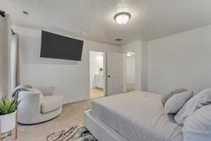 Bedroom featuring baseboards, visible vents, light carpet, and a textured ceiling