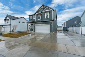 View of front facade featuring a garage, driveway, board and batten siding, and fence