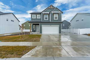 View of front facade with board and batten siding, concrete driveway, fence, and an attached garage