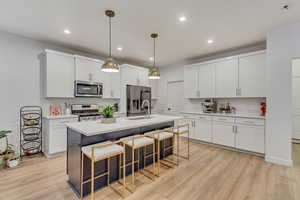 Kitchen featuring light wood-type flooring, stainless steel appliances, a sink, and a kitchen breakfast bar
