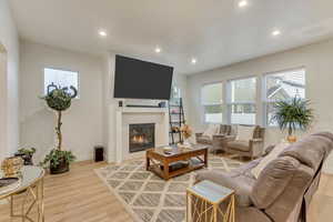 Living area featuring light wood-style floors, a glass covered fireplace, and recessed lighting