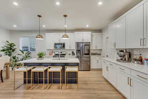 Kitchen featuring a breakfast bar area, appliances with stainless steel finishes, light wood-style floors, white cabinetry, and a sink