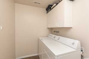 Laundry area featuring washer and dryer, cabinet space, visible vents, and baseboards