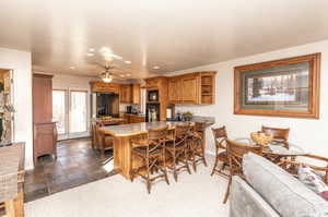 Kitchen with brown cabinets, open shelves, black appliances, a peninsula, and a kitchen bar