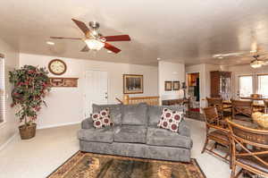 Living room with carpet floors, ceiling fan, a textured ceiling, and baseboards