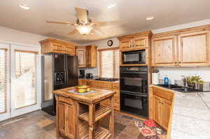 Kitchen featuring stone tile flooring, a sink, black appliances, and ceiling fan