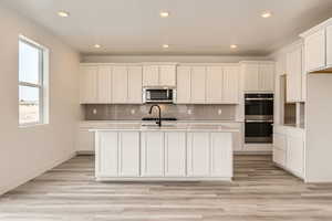 Kitchen with a center island with sink, stainless steel microwave, multiple ovens, and recessed lighting