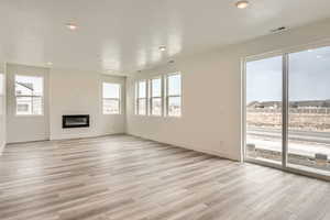 Unfurnished living room featuring a glass covered fireplace, recessed lighting, light wood-type flooring, and baseboards