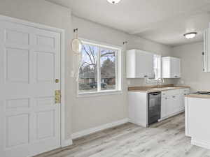 Kitchen with light wood-style flooring, white cabinets, a sink, dishwasher, and baseboards