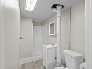 Bathroom with toilet, a walk in shower, wood finished floors, and vanity