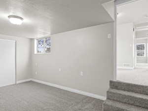 Below grade area featuring a textured ceiling, a wealth of natural light, carpet, and visible vents