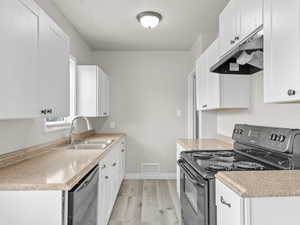 Kitchen with black / electric stove, visible vents, a sink, under cabinet range hood, and dishwashing machine