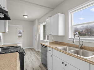 Kitchen with a wealth of natural light, white cabinetry, a sink, under cabinet range hood, and black appliances