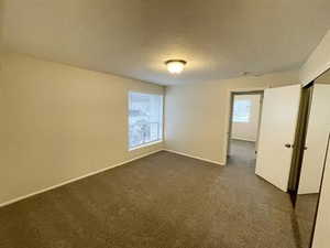 Spare room featuring dark colored carpet, a textured ceiling, and baseboards