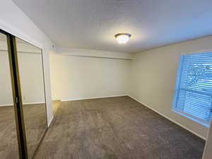 Unfurnished bedroom featuring a textured ceiling, a closet, and carpet