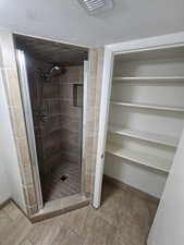 Bathroom with a shower stall, baseboards, a textured ceiling, and stone finish flooring