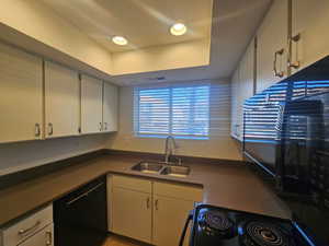 Kitchen with white cabinets, dark countertops, a tray ceiling, black appliances, and a sink