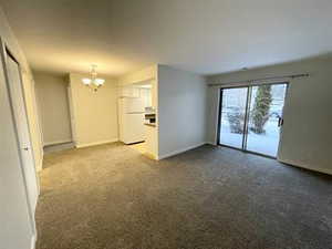 Unfurnished living room with baseboards, dark colored carpet, and an inviting chandelier