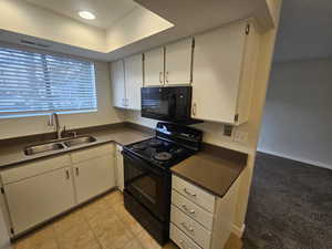 Kitchen with dark countertops, white cabinets, a sink, light tile patterned flooring, and black appliances