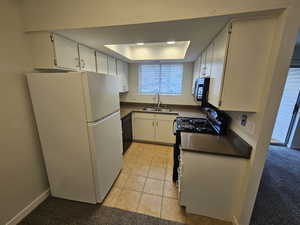 Kitchen with baseboards, a raised ceiling, dark countertops, black appliances, and a sink