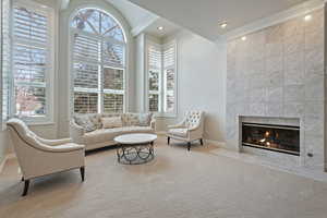 Carpeted living area with a wealth of natural light, a tile fireplace, crown molding, and baseboards