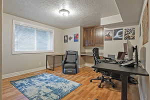 Office space featuring visible vents, baseboards, light wood-style flooring, a textured ceiling, and built in desk